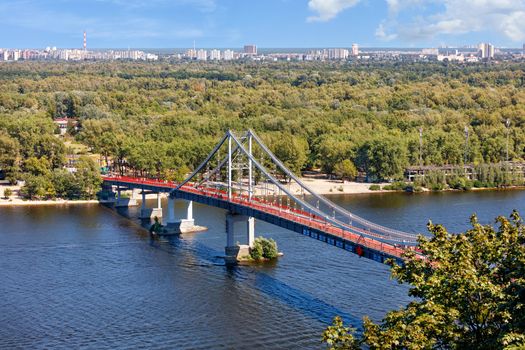 Pedestrian bridge over the Dnipro river to the beach of Trukhaniv island at noon in Kyiv, aerial view, Ukraine.