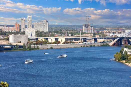 Dnipro river with pleasure boats plying along the city embankment of Kiev on a bright summer day against the background of a beautiful sky and cityscape.