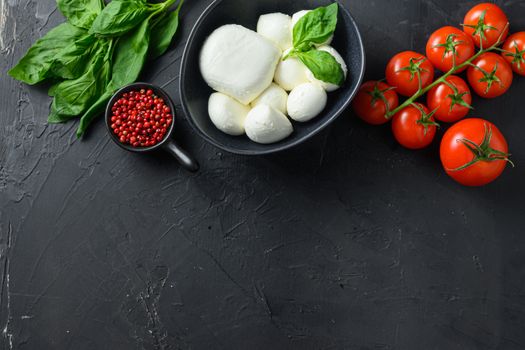 Mini balls of mozzarella cheese,Fresh cherry tomatoes, basil leaf, cheese for caprese salad on black slate stone chalkboard with copyspace. Top view.