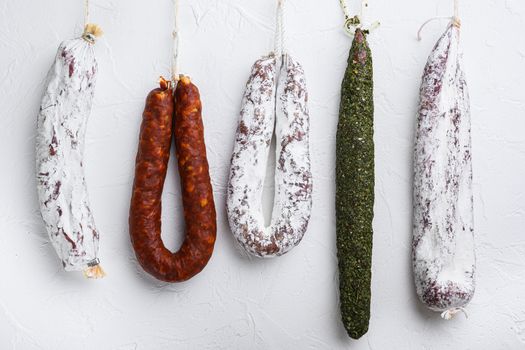 Traditional dry cured sausages meat hanging on white textured background.