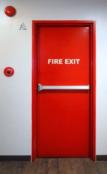 Fire exit emergency door red color metal material with alarm for safety protection and wood floor and white wall in building.