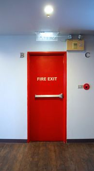 Fire exit emergency door red color metal material with alarm for safety protection and wood floor and white wall in building.