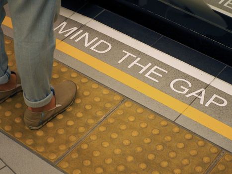 Text sign on floor between train and platform "Mind the gap" with white color and high angle view. 