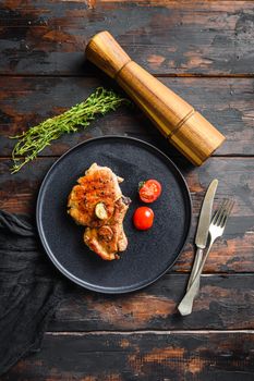 Dish of grilled pork chop with tomatoes top view with knife and fork over old rustic dark wood table table top view vertical