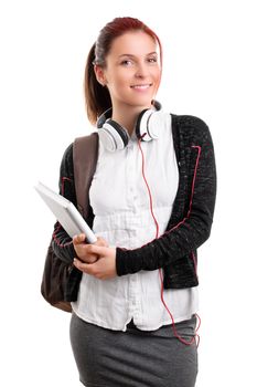 Beautiful smiling young girl in schoolgirl uniform with backpack and headphones, holding a notebook, isolated on white background. Student ready for class. Education concept.