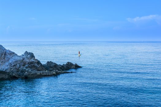 Young man paddling on sup board on calm sea water at Limnionas beach, Greece.