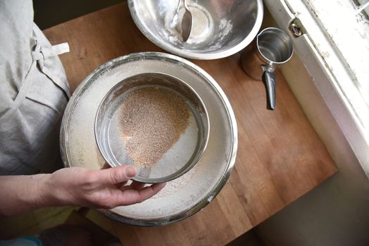 A female cook in apron sifts flour in a metal bowl. Preparing to create a dough for baking. Homemade Patisserie. High quality photo