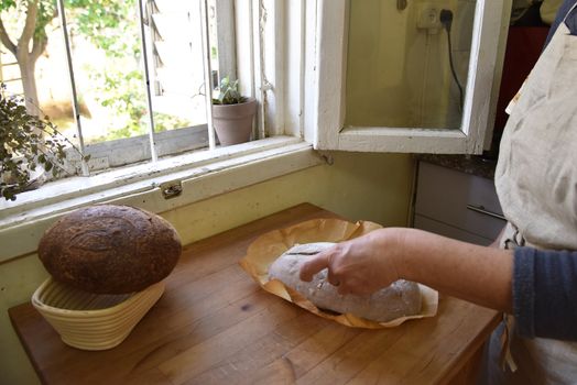 A woman bakes a fresh crusty loaf of homemade bread. Homemade rustic sour bread on a wooden chopping board. Slice of brown bread. Sliced bread. High quality photo