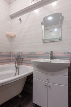 A fragment of the interior of a conventional bathroom with a washbasin and an acrylic bathtub