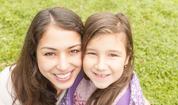 Beautiful and happy young mother with her small daughter outdoors. Both woman and small girl happy and smiling, green grass in background.