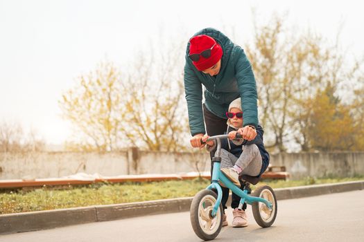 Mother teaches little daughter ride runbike warm autumn day. Young adult parent with kid fun family active leisure. Funny adorable little girl pink sunglasses teaching bike.