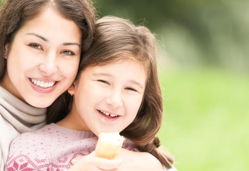 Beautiful and happy young mother with her small daughter outdoors. Both woman and small girl happy and smiling, green park in background.