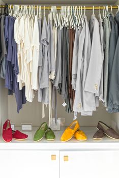 Row of new casual clothing on hangers at shop with four colorful pairs of shoes under it. Clothes presented as in wardrobe. Apparel ready for sale. Going shopping. Trade and commerce.