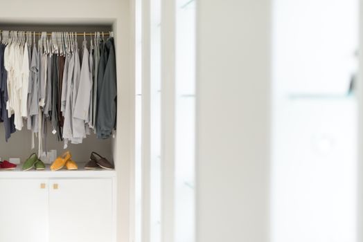 Row of new casual clothing on hangers at shop with four colorful pairs of shoes under it. Clothes presented as in wardrobe. Apparel ready for sale. Going shopping. Trade and commerce.