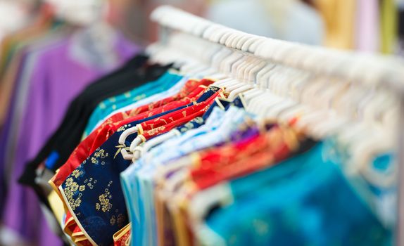 Rows of new colorful clothing on hangers at shop in foreground and background. Great choice of casual clothes of different colors. Apparel ready for sale. Going shopping. Trade and commerce.