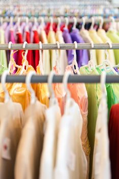 Rows of new colorful clothing on hangers at shop in foreground and background. Great choice of casual clothes of different colors. Apparel ready for sale. Going shopping. Trade and commerce.