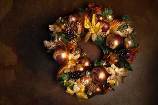 Christmas wreath on brown background with copyspace. Wreath decorated with balls and bows of gold and brown, with green leaves. Luxury New Year decor