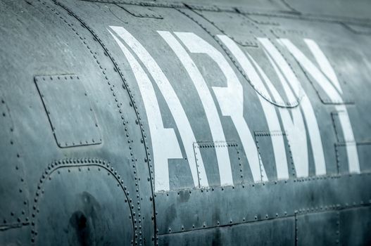Close-up side view of military airplane with big white army inscription. Old war aircraft in metal plates. Military aviation. Retro and grungy view. Safety and protection.