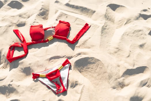 Red female swimwear on soft sand. Holidays and vacations concept. Sunbathing and relaxation on beach on hot sunny day. Summer background. Swimsuit advertising.
