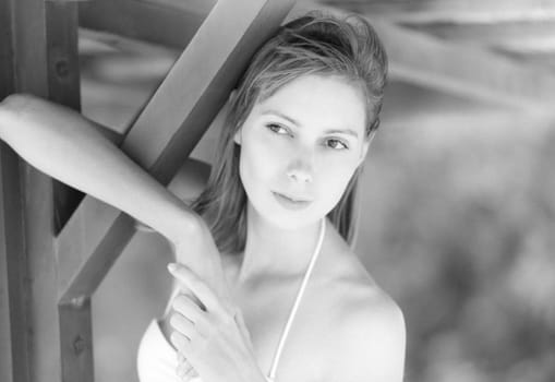 Pretty girl standing under wooden pier and smiling. Beautiful young woman on beach. Green trees in background. Leisure activity outdoor. Idea of summer vacation. Black and white with grain added.