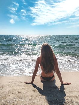 Back view portrait of a Girl who sunbather relaxing sitting on the sand of the beach on summer vacation