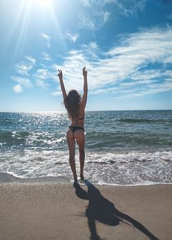 back view of slim young woman posing in bikini near the sea on resort