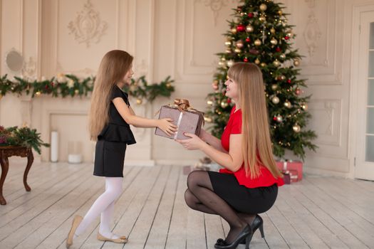 Little girl gives her mom a box with a Christmas present.