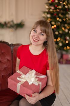 Portrait of a beautiful blonde girl with a Christmas gift near the Christmas tree.