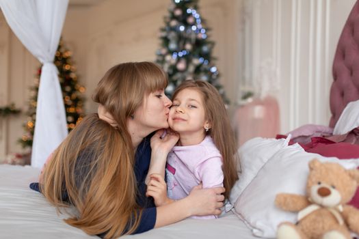 Little girl spends time playing with mom while lying in bed. Christmas tale. Happy childhood.