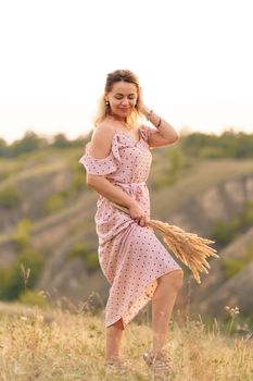 Beautiful tender girl in a white sundress walks at sunset in a field with a spikelet bouquet