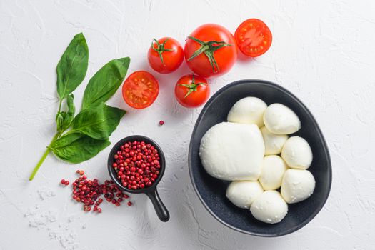 Raw ripe Mozzarella cheese balls with fresh basil leaves and cherry tomatoes, the ingredients , on white background top view.