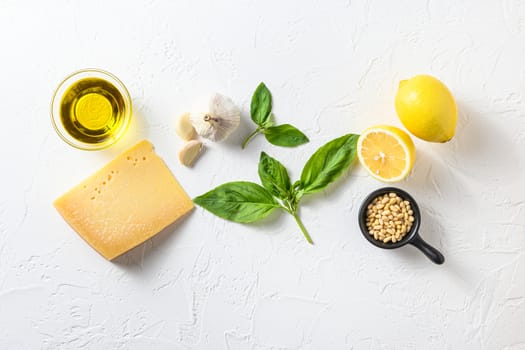 Genovese pesto ingredients concept or ingredients Parmesan cheese, basil leaves, pine nuts, olive oil, garlic, salt, pepper and mortar for cooking on white old stone table top view with copy space.