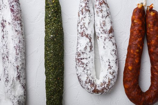 Traditional dry cured sausages meat hanging on white textured background.