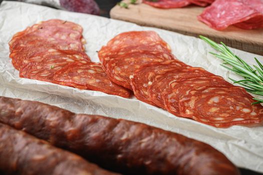 Variety of dry cured chorizo, fuet and other sausages cut in slices with herbs on old wooden table.