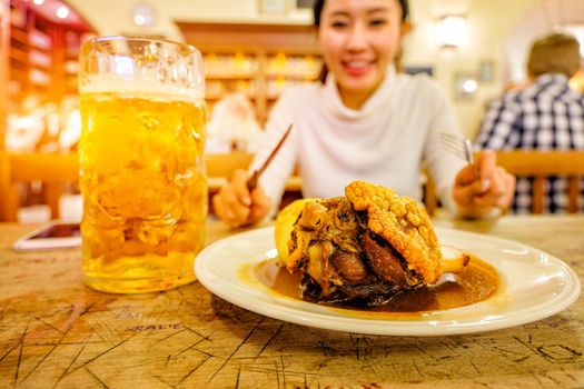 Cute girl drinking beer and pork knuckle in Hofbraeuhaus beer house, Munich, Bavaria, Germany