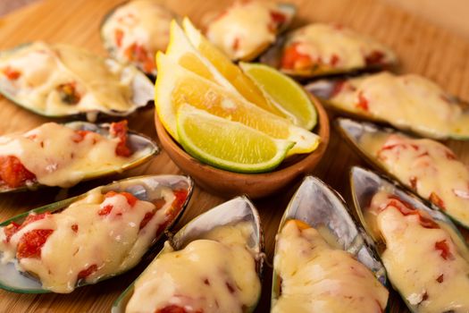 Seafood. Mussel clams. Baked greenshell mussels with tomato and cheese, cilantro and lemon on wooden background