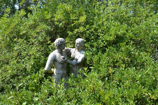 Adam and Eve statue with apple and green plants or bushes