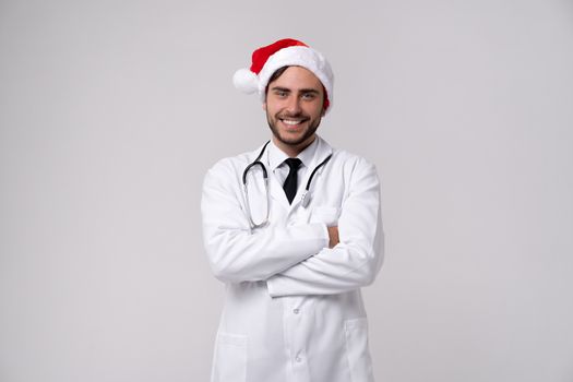 Young handsome doctor in white uniforme and Santa Claus hat standing in studio on white background loking in camer and teeth smile Portrait medical student Christmas New Year Holiday Medicine concept