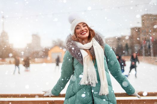 Beautiful lovely middle-aged girl curly hair warm winter jackets white knitted hat glove stands ice rink background Town Square Christmas mood lifestyle Happy holiday woman snowy day Winter leisure