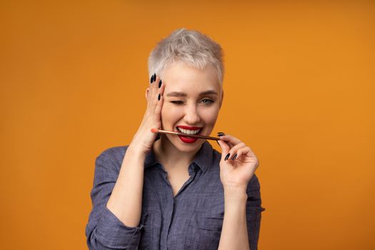 Close up portrait makeup artist. Make up courses. Concept of self visage masterclasess. Fashion professional. Woman hold makeup brushes on the hands. Studio shot on the orange color background