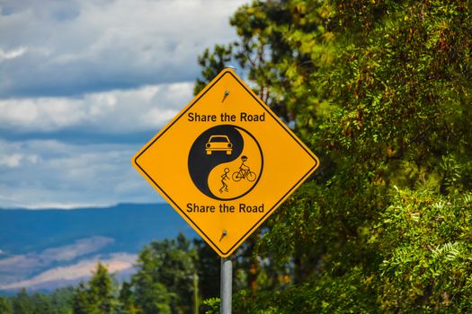 Share the Road yellow sign on green leaves and blue sky background