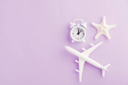 World Tourism Day, Top view flat lay of minimal toy model plane, airplane, starfish, alarm clock and compass, studio shot isolated on a purple background, accessory flight holiday concept