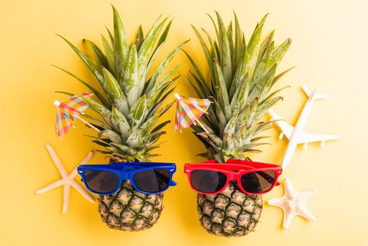 Celebrate Summer Pineapple Day Concept, Top view flat lay of funny two pineapples in sunglasses with model plane and starfish, studio shot isolated on yellow background, Holiday summertime in tropical