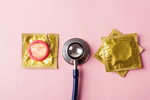 World sexual health or Aids day, Top view flat lay medical equipment, condom in pack and stethoscope, studio shot isolated on a pink background, Safe sex and reproductive health concept