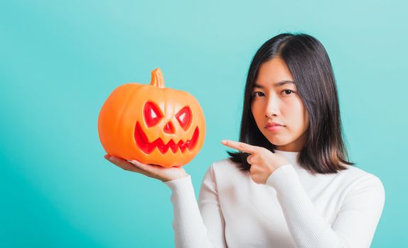 Portrait of Asian beautiful young woman holding orange model pumpkins, funny happy female with ghost pumpkins, studio shot isolated on blue background