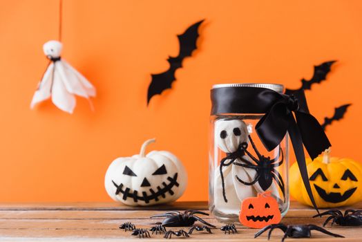 Funny Halloween day decoration party, Baby white ghost crafts scary face in jar glass and cute pumpkin ghost on wood table, studio shot isolated on orange background have spider and bats