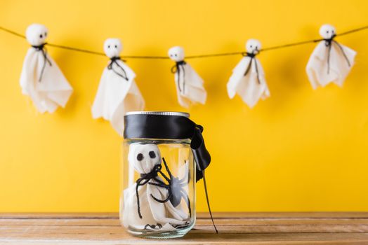 Funny Halloween day decoration party, Cute white ghost crafts scary face hanging on background have only one baby ghost in jar glass, isolated yellow, Happy holiday DIY handicraft concept