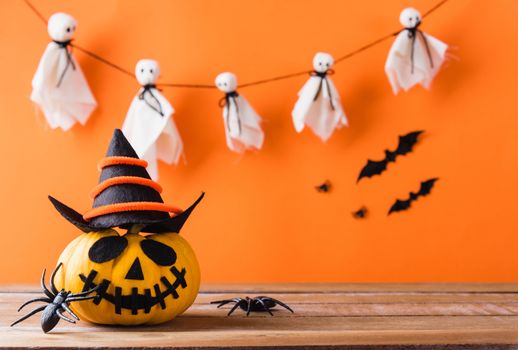 Funny Halloween day decoration party, Cute pumpkin ghost spooky jack o lantern face wear hat, black spider and bats on wooden table, studio shot isolated on an orange background, Happy holiday concept