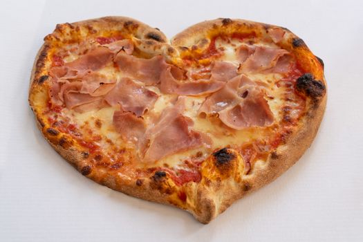 Heart shaped pizza with tomatoes and ham for Valentines Day on white cardboard background,Food concept of romantic love