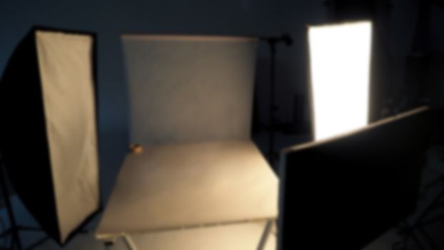 Blurry image behind the scenes of shooting video production in a studio with small set professional lighting equipment.